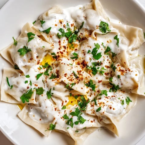 Steaming Turkish Cheesy Manti, plump dumplings with a vibrant swirl of spiced butter and fresh parsley.