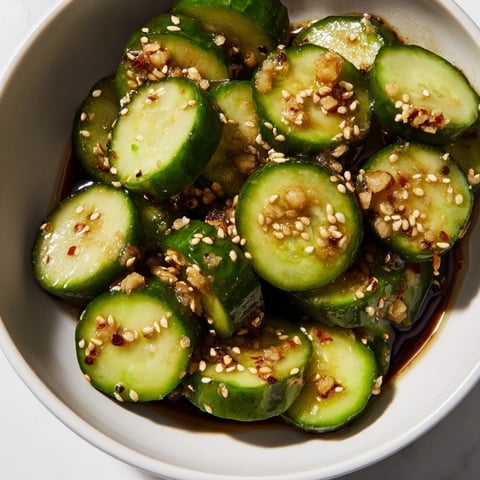 Bright green cucumber rounds glisten with a savory garlic soy glaze, topped with sesame seeds and green onions, ready for serving.