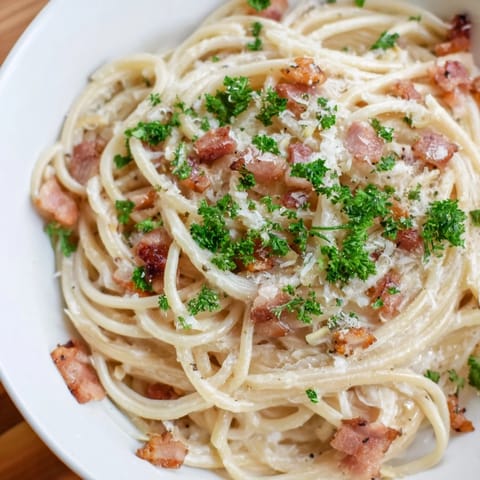 Golden, crispy bacon bits topping a steaming plate of creamy garlic bacon pasta, ready to eat.