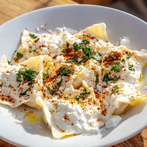 Golden, perfectly-cooked Turkish Cheesy Manti: tender dough pillows atop creamy yogurt sauce ready to eat.