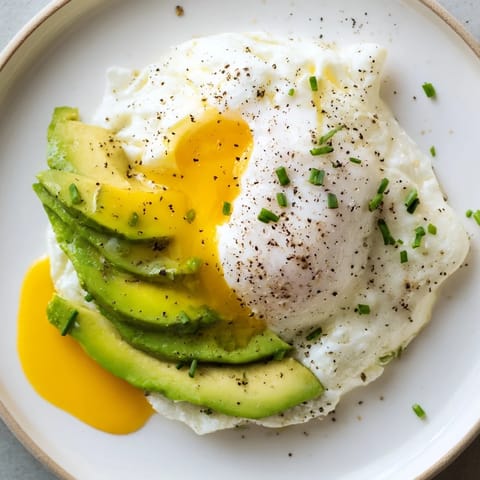 Golden baked Cloud Bread Breakfast Clouds with runny poached egg yolks and ripe avocado, garnished with fresh chives.
