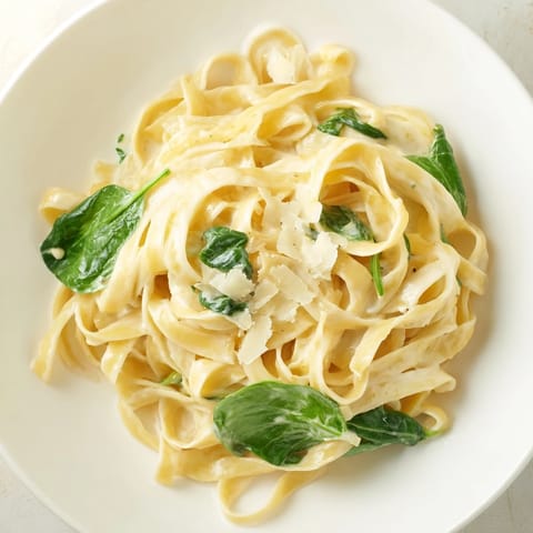 A close-up of creamy garlic spinach pasta, garnished with parsley and grated Parmesan for a comforting weeknight meal.