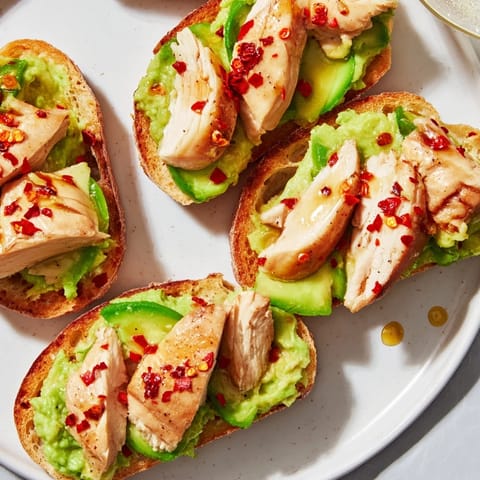 A close-up of Smashed Avocado Chicken Toast with crispy sourdough, avocado mash, sliced chicken, and fresh cilantro on a rustic board.  
