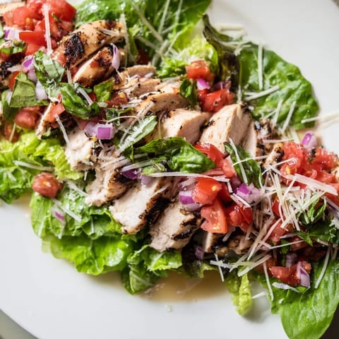 Bright, fresh Bruschetta Chicken Salad features tender grilled chicken, a zesty tomato-basil topping, and crisp greens, served with lemon wedges for a light and flavorful meal.