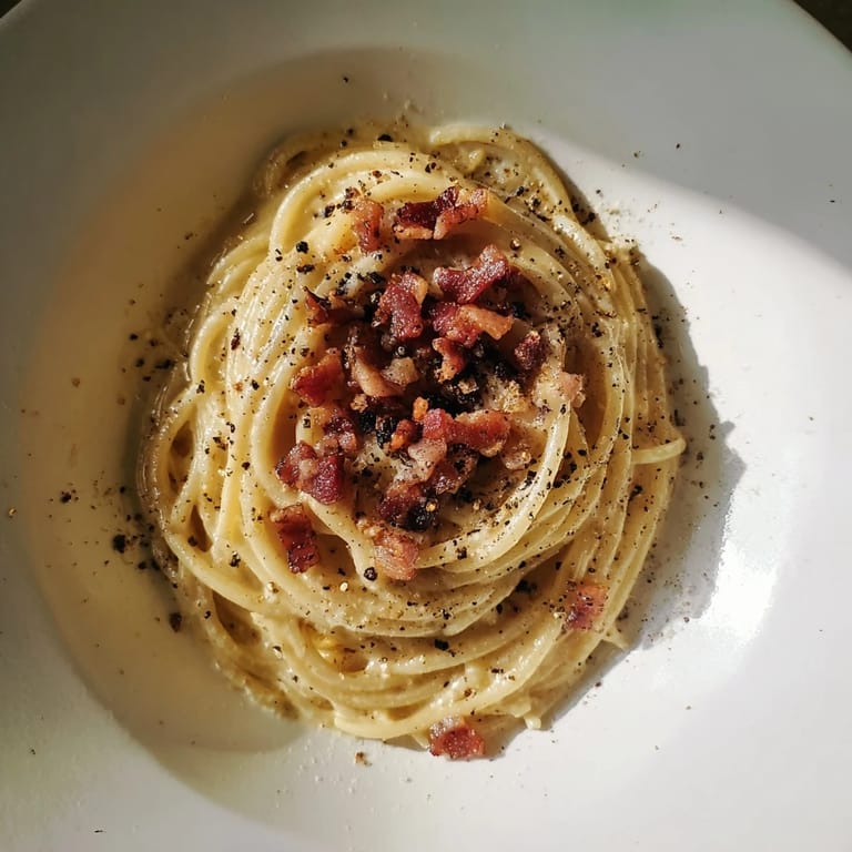 A close-up of Express Spaghetti Carbonara shows strands of pasta clinging to crispy bacon, garnished with pepper.