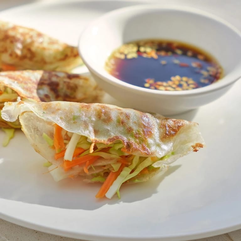 Stack of hot Crispy Rice Paper Dumplings alongside chopsticks and a flavorful sesame-soy dipping sauce on a rustic kitchen table.
