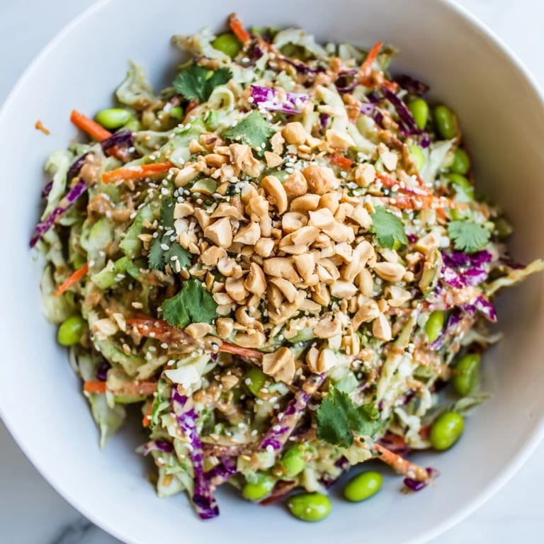 A close-up of the Crunchy Thai Peanut Salad shows chopped peanuts and sesame seeds sprinkled over vibrant vegetables, with fresh lime wedges on the side.