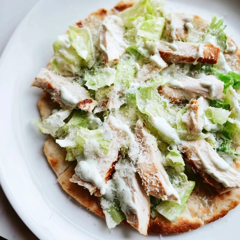 Golden-brown flatbread loaded with tender grilled chicken, crisp romaine, and Caesar dressing, garnished with fresh parmesan on a rustic kitchen table.