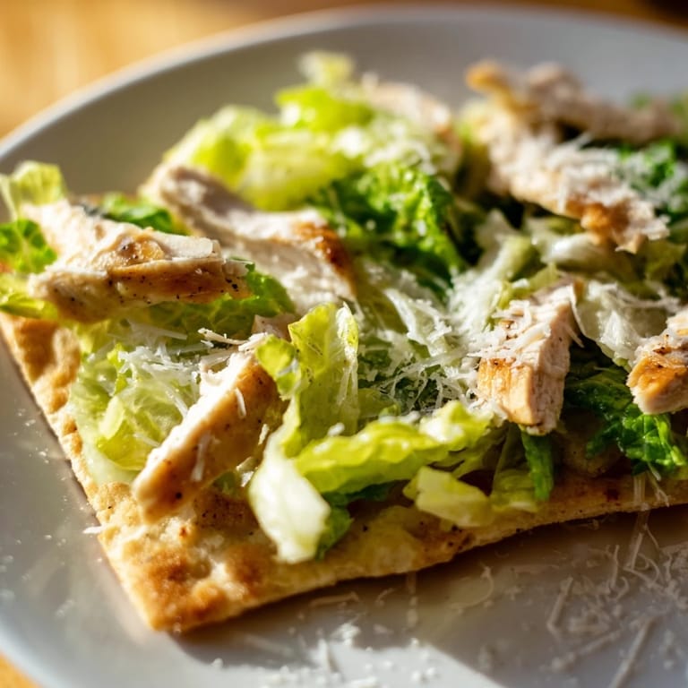 Freshly baked Chicken Caesar Flatbread with grilled chicken slices, tangy dressing, and crisp lettuce, served alongside optional cherry tomatoes and a light white wine.